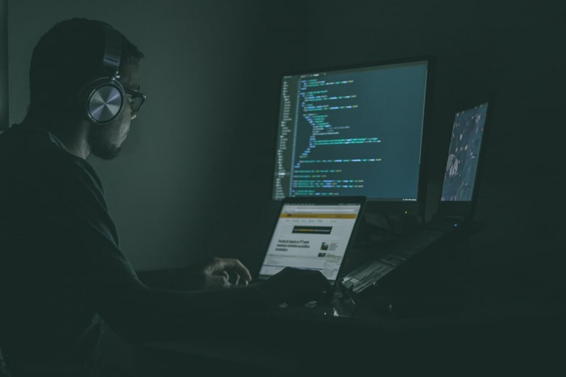 Hacker sitting in the dark using computer to commit tech fraud