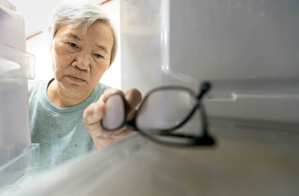 A senior woman with memory impairment is storing her glasses in the fridge.